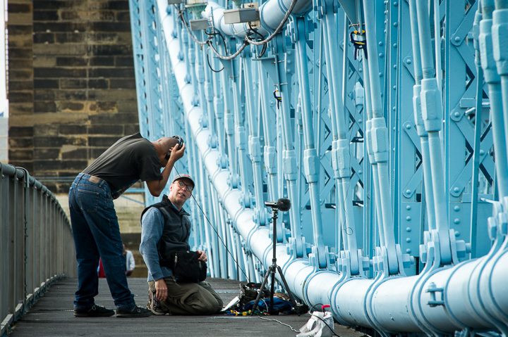 Sound recordist Richard Alan Hannon lends his headphones to a curious pedestrian along the John A. Roebling Suspension Bridge while recording May 2, 2016. The bridge spans the Ohio River between Cincinnati, Ohio and Covington, Kentucky. Photo by Adam Lau.